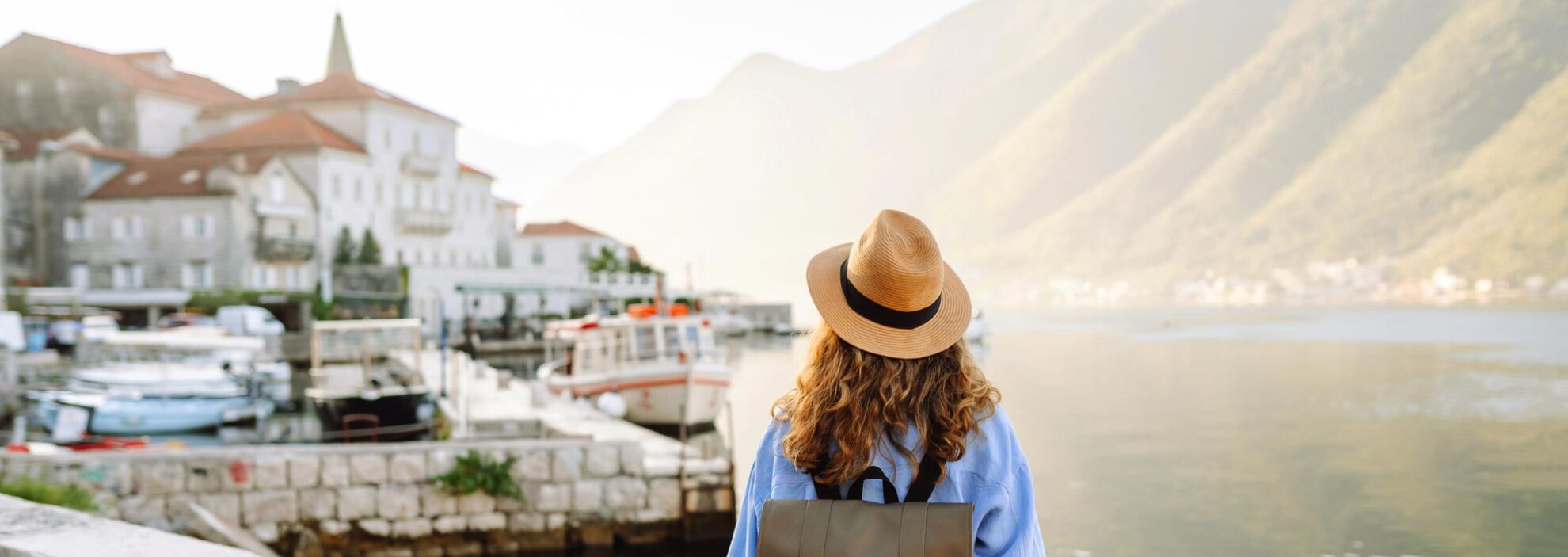 Frau mit Rucksack sieht auf eine malerische Küstenstadt und Berge am Wasser.