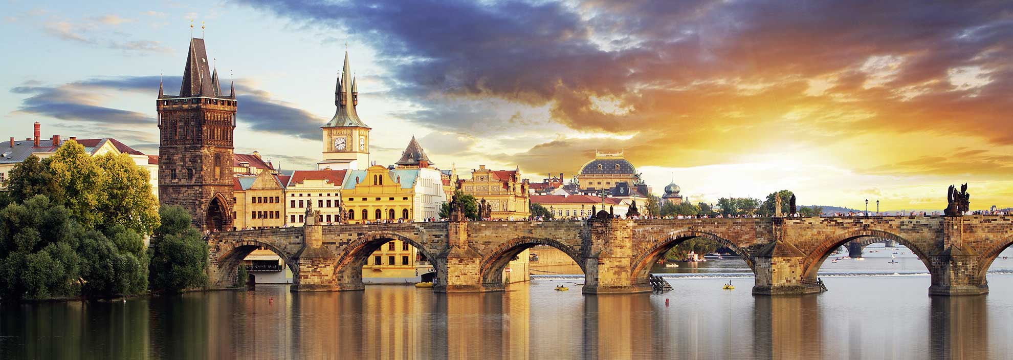 Steinbrücke über Fluss in Sonnenuntergangsstimmung, historische Gebäude im Hintergrund.